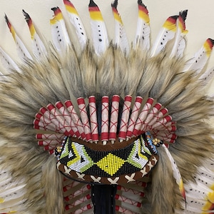 May include: A Native American headdress with a brown base and a beaded design. The headdress is adorned with white and red feathers, and a long, brown fur trim.