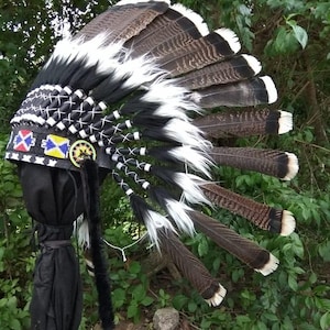 Pode incluir: Um cocar nativo americano tradicional em preto, branco e castanho. O cocar é adornado com penas, contas e costuras intrincadas. As penas têm pontas brancas e castanhas, criando um contraste marcante. Um símbolo da herança cultural.