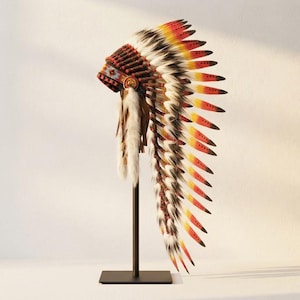 Op de afbeelding: Een decoratieve hoofdtooi met een band met rode, blauwe en witte geometrische patronen. De kroon is versierd met lange, gelaagde veren die verlopen van wit aan de basis naar gele, oranje en zwarte punten, met accenten van wit bont aan de zijkanten.