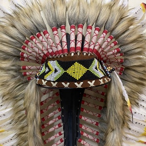 May include: A brown and black beaded headdress with white and yellow feathers. The headdress has a brown leather band with a beaded design and a red and white fringe.