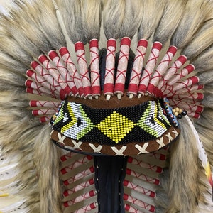 May include: A Native American headdress with white feathers, red and white trim, and a beaded band with yellow and black accents.
