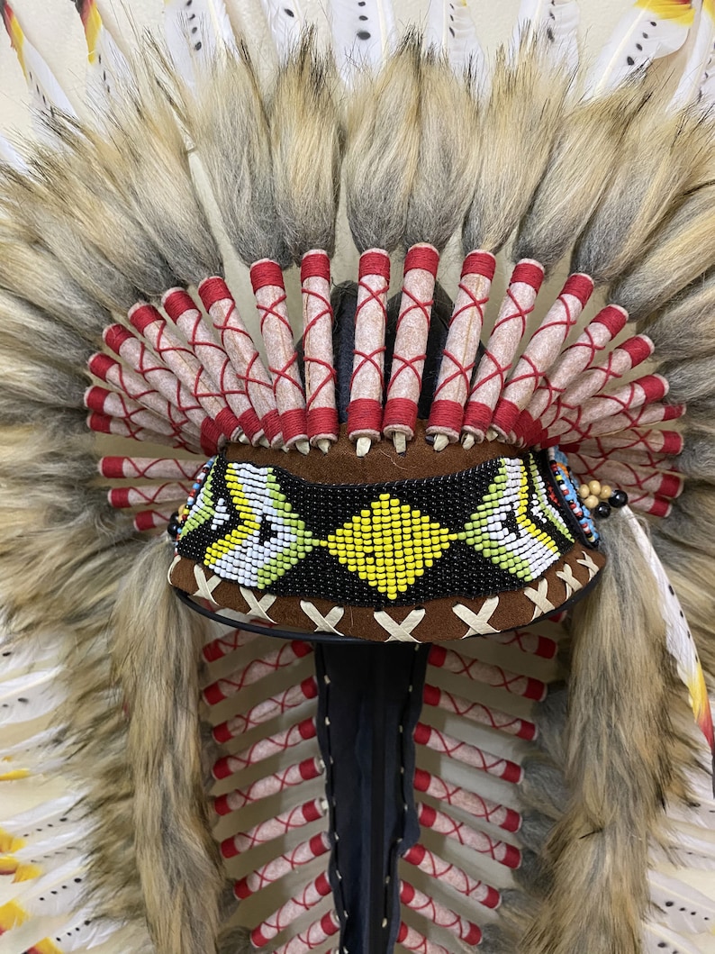 May include: A Native American headdress with white feathers, red and white trim, and a beaded band with yellow and black accents.
