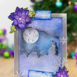 May include: A framed winter-themed art piece with a silver border. The artwork features a snowy landscape with a full moon and the words "Ho Ho Ho". Embellished with purple poinsettias, snowflakes, and the words "Happy" and "Holidays".