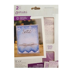 May include: A Gemini Delicate Snowfall embossing folder set. The package includes a 5" x 5" (12.7cm x 12.7cm) embossing folder and a cut and emboss folder. The card features the text "Let it Snow" with a snowflake design.