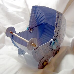 May include: A blue and white paper baby carriage with a white ribbon and a white bow. The carriage has a white and blue striped pattern and a white and blue floral design.
