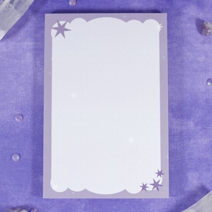 May include: A purple notepad with a white cloud-shaped border and a dotted pattern. The notepad has a star design in the top left corner and a star design in the bottom right corner.