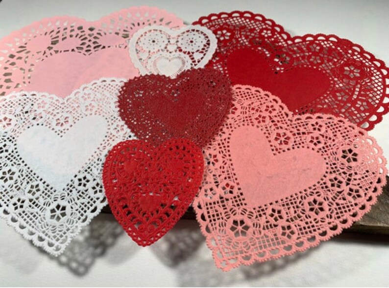 Peut inclure: Assortiment de napperons en dentelle en forme de c&oelig;ur en rose, blanc et rouge. Les napperons sont faits de dentelle d&eacute;licate et ont un bord festonn&eacute;.