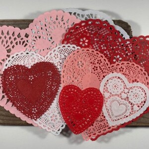 Peut inclure: Une collection de doilies en papier rouge, rose et blanc en forme de c&oelig;ur. Les doilies sont dispos&eacute;s en forme de c&oelig;ur sur une surface en bois.