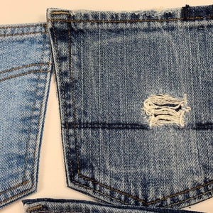 May include: Two pieces of blue denim fabric with a distressed pocket. The pocket has a small hole in the center.