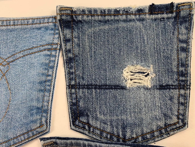 May include: Two pieces of blue denim fabric with a distressed pocket. The pocket has a small hole in the center.
