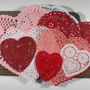 Peut inclure: Une collection de doilies en papier rouge, rose et blanc en forme de c&oelig;ur. Les doilies sont dispos&eacute;s en forme de c&oelig;ur sur un morceau de bois vieilli.