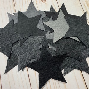May include: A pile of black, gray, and dark gray denim fabric stars. The stars are all the same size and shape, and they are arranged in a random pattern.