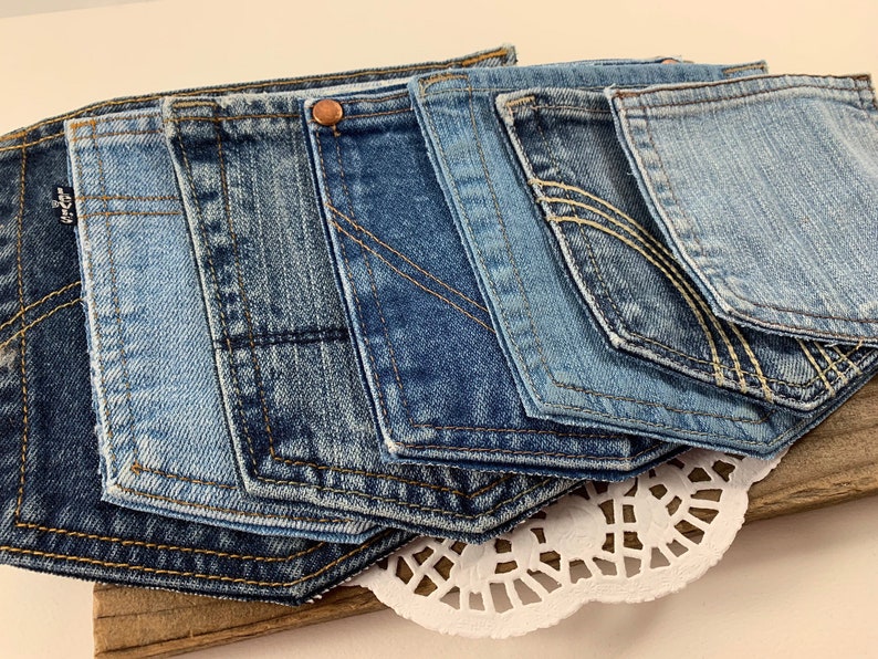 May include: A collection of seven denim pockets in various shades of blue, arranged in a staggered pattern. The pockets are sewn together and have a raw edge finish.