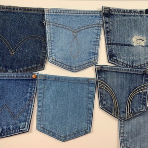 May include: A collection of seven blue denim jean pockets, each with a different style of stitching. The pockets are arranged in a random pattern on a white background.