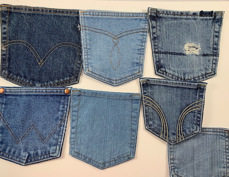 May include: A collection of seven blue denim jean pockets, each with a different style of stitching. The pockets are arranged in a random pattern on a white background.