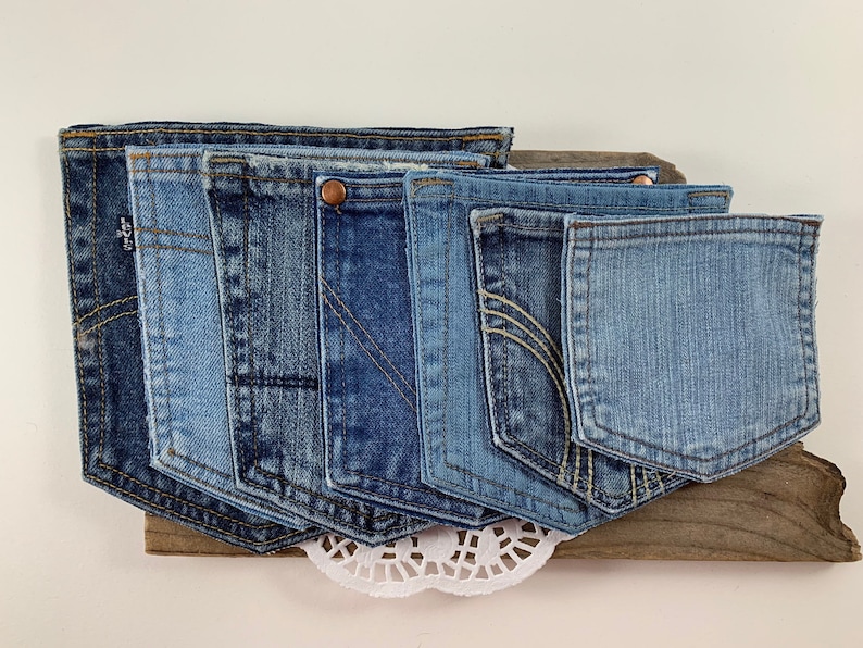May include: A collection of blue denim jean pockets arranged in a row on a piece of driftwood. The pockets are all different sizes and shapes, and they have been sewn together to create a unique wall hanging.