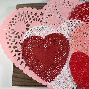Peut inclure: Une collection de doilies en papier rose, blanc et rouge en forme de c&oelig;ur. Les doilies sont dispos&eacute;es en couches sur une surface en bois.