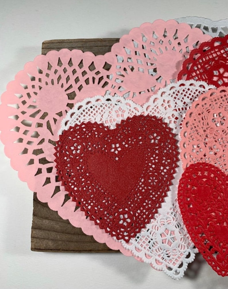 Peut inclure: Une collection de doilies en papier rose, blanc et rouge en forme de c&oelig;ur. Les doilies sont dispos&eacute;es en couches sur une surface en bois.