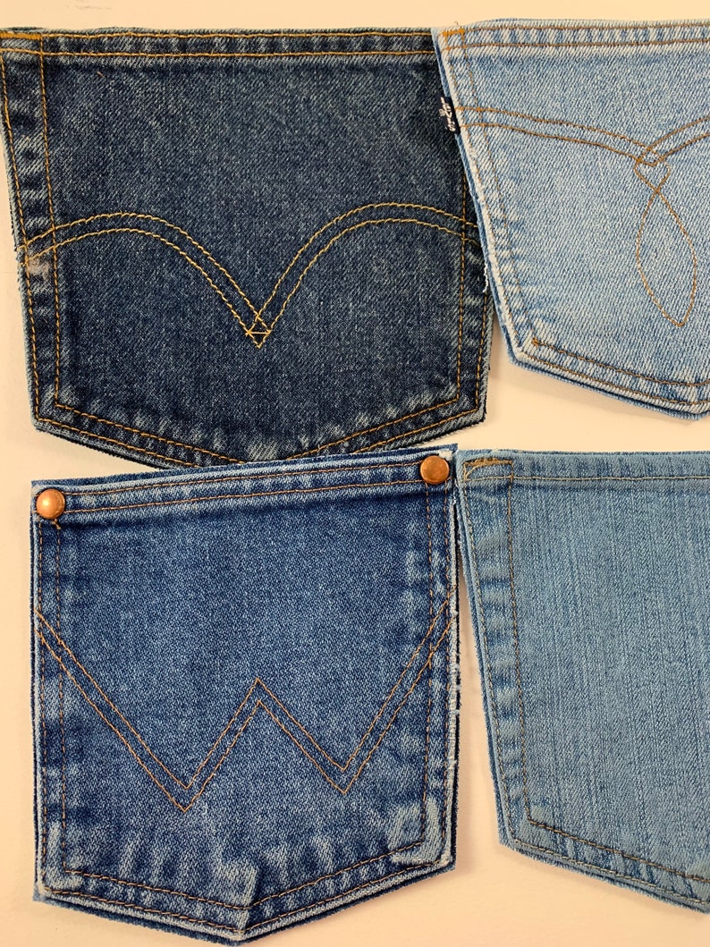May include: Four different denim jean pockets with contrasting stitching. The pockets are all blue, but the shades of blue vary. The pockets have different stitching designs, including a classic curved design and a more modern zig-zag design.