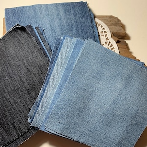 May include: A stack of denim fabric squares in various shades of blue and black. The fabric is arranged in a pile, with the darkest blue fabric on the bottom and the lightest blue fabric on top.