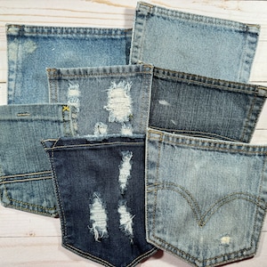 May include: A collection of six denim jean pockets in various shades of blue, some with distressed details and frayed edges. The pockets are arranged in a stack, with the top pocket being the largest and the bottom pocket being the smallest.