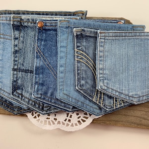May include: A set of seven blue denim jean pockets, sewn together to create a decorative wall hanging. The pockets are arranged in a staggered pattern, with the largest pocket at the bottom and the smallest pocket at the top.