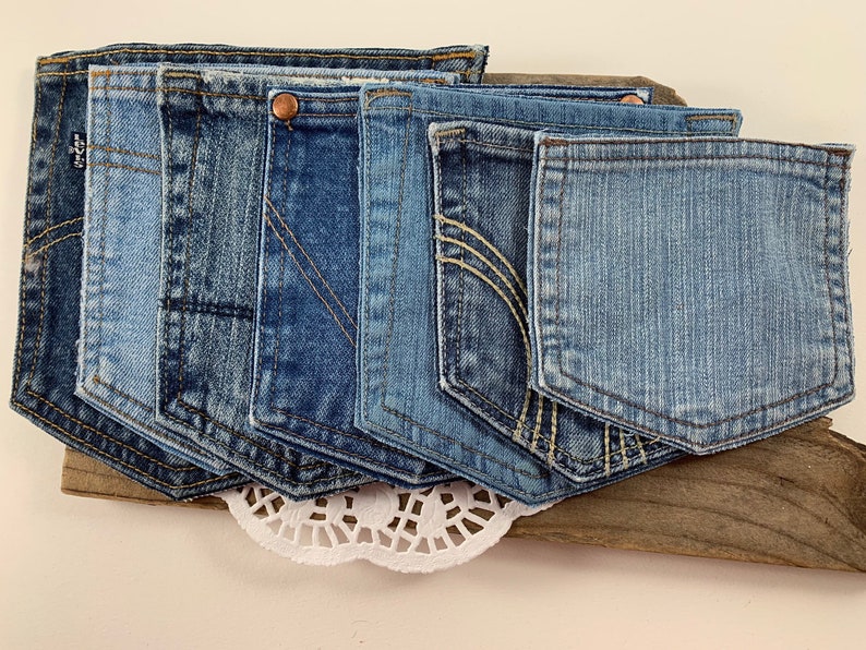 May include: A set of seven blue denim jean pockets, sewn together to create a decorative wall hanging. The pockets are arranged in a staggered pattern, with the largest pocket at the bottom and the smallest pocket at the top.