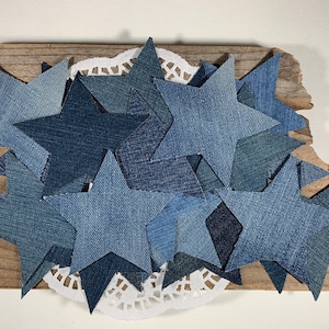 May include: A collection of denim blue star shapes arranged on a piece of weathered wood with a white doily underneath.