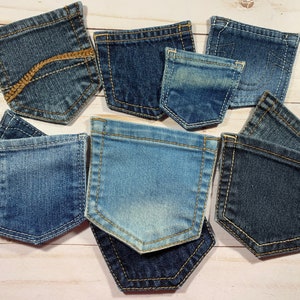 May include: A collection of denim jean pockets in various shades of blue. The pockets are arranged on a light wood-grain surface. Some pockets have decorative stitching and unique fading patterns, showcasing the texture of the denim.