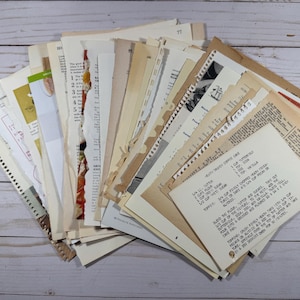 May include: A collection of vintage recipe cards and pages from cookbooks, featuring handwritten and printed text. The papers vary in color from cream to tan, with some showing signs of age and wear. The pages are arranged in a fan shape, suggesting a curated collection.