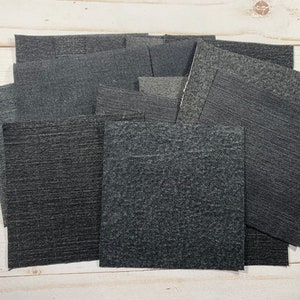 May include: A collection of dark gray fabric squares with a textured surface. The fabric squares are arranged in a random pattern.