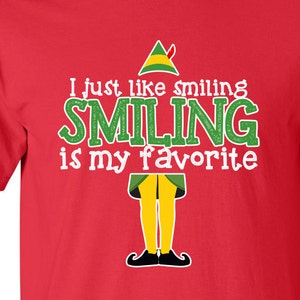 May include: Red t-shirt featuring a green elf character and the text "I just like smiling SMILING is my favorite".