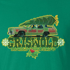 Peut inclure: Un t-shirt vert avec une illustration de style vintage d'une voiture familiale avec un sapin de Noël sur le toit. Le texte "Griswold Family Christmas" est imprimé sous la voiture.