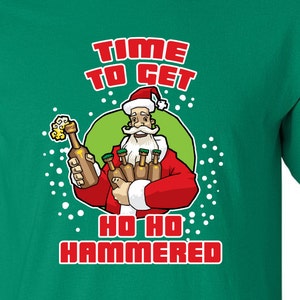Peut inclure: T-shirt vert avec une image de dessin animé du Père Noël tenant des bouteilles de bière. Le texte sur le t-shirt est "Time to get Ho Ho Hammered."