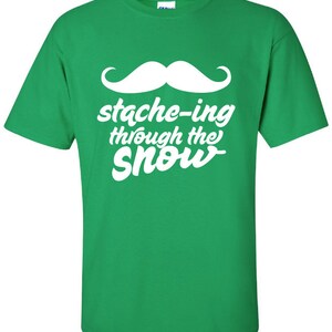 May include: Green t-shirt with a white mustache and the text "stache-ing through the snow".