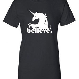 Puede incluir: Camiseta negra con una silueta de unicornio blanca y la palabra "believe" impresa en la parte delantera.