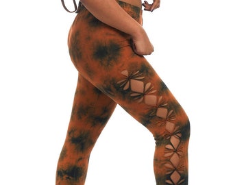 May include: A two-piece activewear set in a tie-dye pattern of orange and dark green. The set includes a halter-style crop top and leggings with cut-out diamond shapes along the sides. The model is wearing the outfit.