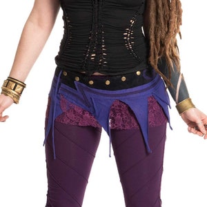 May include: A woman wearing a black, crocheted top with a purple and blue skirt and leggings. She has dreadlocks and is wearing gold jewelry.