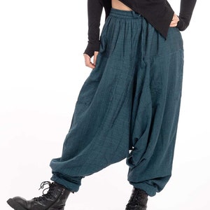Pode incluir: Uma mulher vestindo uma camisa preta de manga comprida e calças soltas azul-esverdeadas. Ela está usando botas pretas com cadarços.