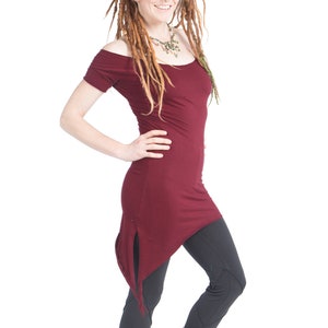 May include: A burgundy off-the-shoulder tunic top with a unique asymmetrical hemline, paired with dark gray leggings and red and black patterned boots. The outfit is styled with a necklace.