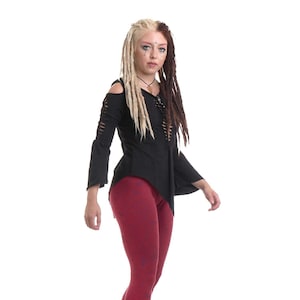 Könnte beinhalten: Eine Frau mit blonden und braunen Dreadlocks trägt ein schwarzes, asymmetrisches, langärmeliges Shirt mit einem Schnürdetail vorne. Sie trägt außerdem rote Leggings und schwarze Plateauschuhe.