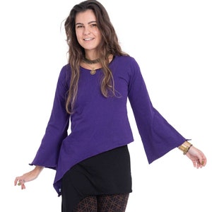 Puede incluir: Una mujer con una camisa de manga larga morada con una falda asimétrica negra y leggings marrones con estampado. La camisa tiene un cuello alto y las mangas son acampanadas.