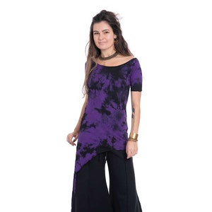 Op de afbeelding: Een vrouw draagt een paars en zwart tie-dye top met een zwarte off-shoulder halslijn en een zwarte rok.