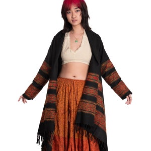 Puede incluir: Una mujer con un chal negro y rojo estampado sobre un top blanco corto y una falda larga naranja y marrón.