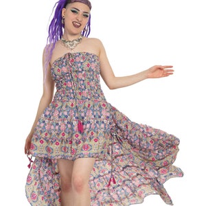 May include: A woman wearing a strapless high-low floral print dress with a pink and blue color scheme. The dress has a fitted bodice and a flowing skirt with a high-low hemline. She is wearing colorful sneakers with pink laces.