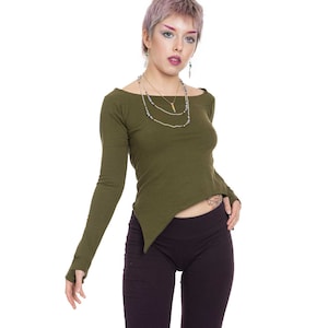 Puede incluir: Una mujer con una camisa verde de manga larga con un dobladillo diagonal y pantalones de color morado oscuro. Lleva un collar de capas con un pequeño colgante.