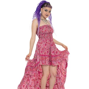 May include: A woman with purple hair wearing a pink and white floral print maxi dress with a high-low hemline. She is wearing silver platform sandals.