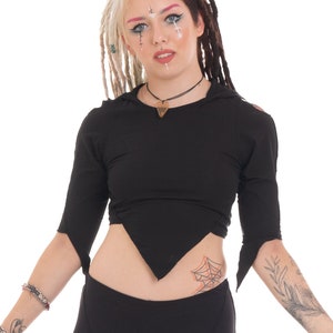 Peut inclure: Une femme portant un haut court noir avec une ourlet triangulaire et un legging noir. Elle a les cheveux bicolores, un côté blond et l'autre côté brun foncé. Elle porte un collier avec un pendentif en forme de cœur.