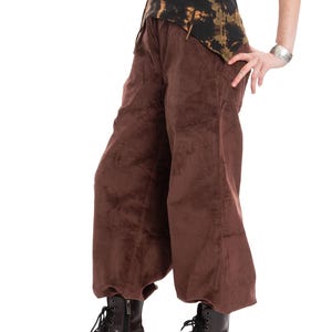 May include: A person wearing a black and brown tie-dye top and wide-leg brown corduroy trousers. The person is also wearing dark brown platform boots with black laces. A silver bracelet is visible on the wrist.