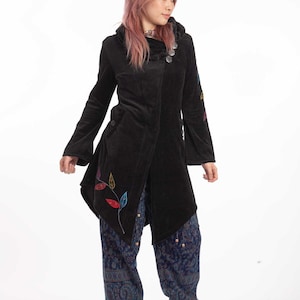 May include: A black velvet coat featuring an asymmetrical hem, a hood, and decorative silver buttons at the neckline. The coat is adorned with colorful embroidered leaf motifs on the lower front and sleeve. Paired with blue patterned trousers.